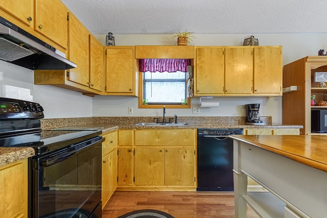 kitchen with black appliances, under cabinet range hood, a sink, a textured ceiling, and light wood-style floors