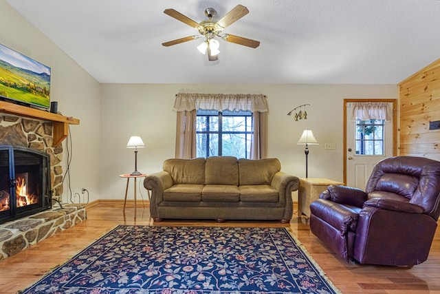 living room with a ceiling fan, a textured ceiling, wood finished floors, a fireplace, and baseboards