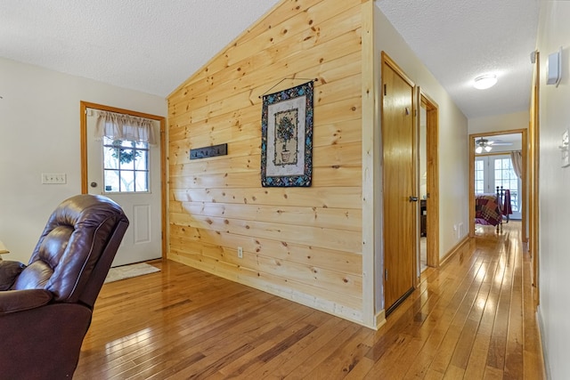 foyer featuring vaulted ceiling, a healthy amount of sunlight, light wood-type flooring, and wood walls