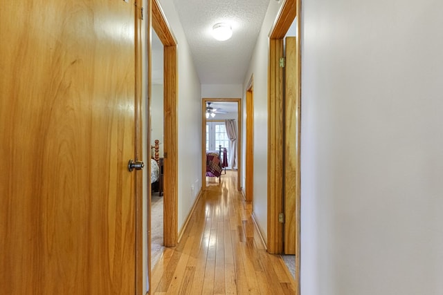 corridor with baseboards, a textured ceiling, and light wood-style floors