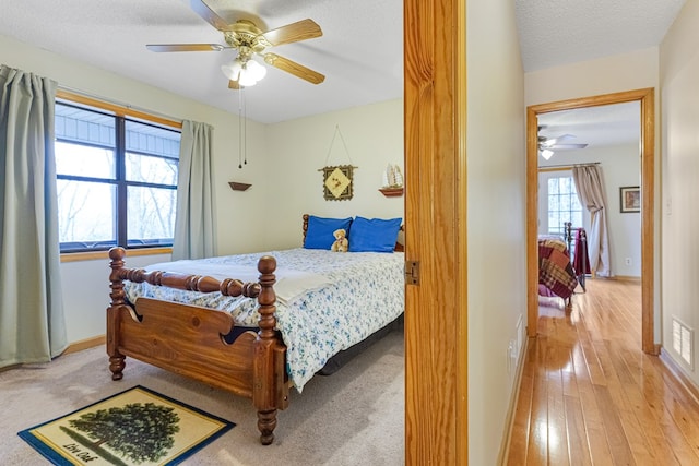 bedroom with hardwood / wood-style floors, visible vents, baseboards, ceiling fan, and a textured ceiling