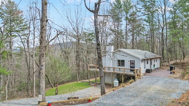 view of front of home featuring a forest view, gravel driveway, a deck, and a chimney