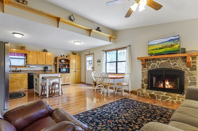 living area with a ceiling fan, baseboards, light wood-style flooring, a fireplace, and a textured ceiling