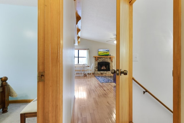 corridor with an upstairs landing, hardwood / wood-style floors, baseboards, and vaulted ceiling