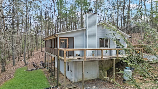 rear view of house with driveway, a wooden deck, an attached garage, a sunroom, and a chimney