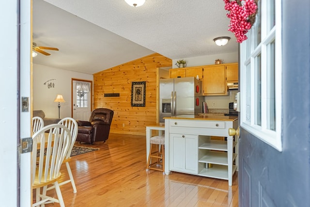 kitchen with wooden walls, stainless steel fridge with ice dispenser, under cabinet range hood, open floor plan, and light wood-style flooring