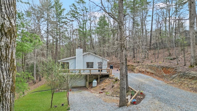 chalet / cabin featuring gravel driveway, a front yard, a chimney, a garage, and a deck