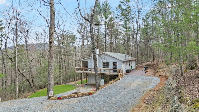 view of front facade with a view of trees, gravel driveway, a deck, and a chimney