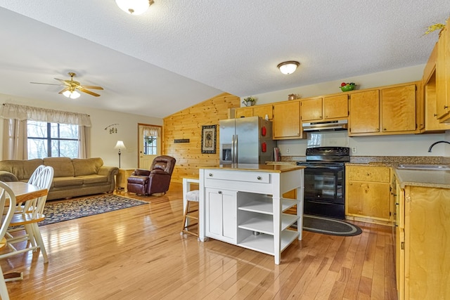 kitchen featuring stainless steel refrigerator with ice dispenser, a sink, under cabinet range hood, black range with electric cooktop, and wood walls