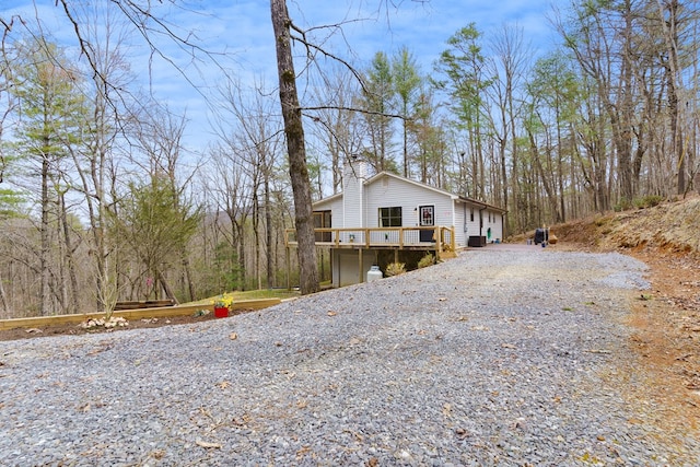 view of side of home featuring a wooden deck, gravel driveway, and a chimney