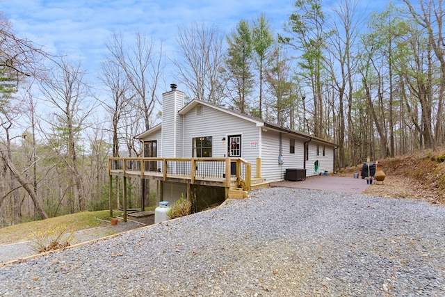 view of front facade featuring central AC, driveway, a chimney, and a deck