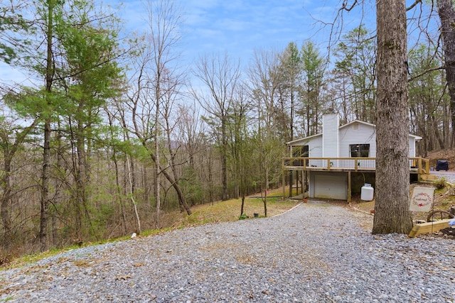 view of yard featuring a garage, gravel driveway, a deck, and a wooded view