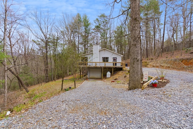 exterior space with a deck, driveway, a forest view, a garage, and a chimney