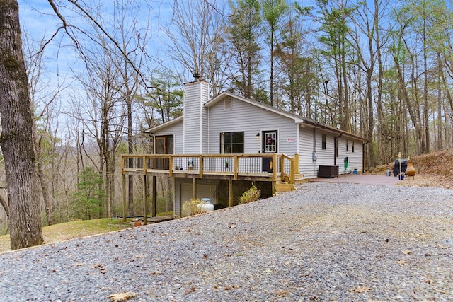 view of property exterior featuring a wooden deck, a chimney, central AC, and driveway