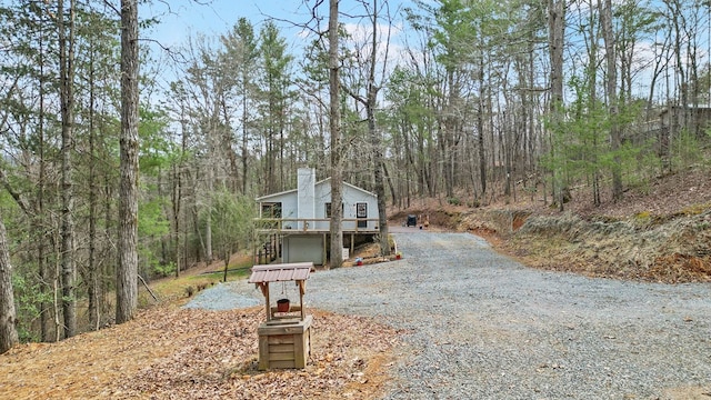 view of front facade featuring an attached garage, a chimney, gravel driveway, and a forest view