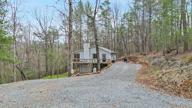 view of side of property with a forest view, gravel driveway, a deck, and a chimney