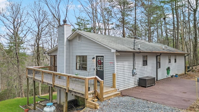 rear view of house featuring a shingled roof, a patio area, a chimney, and a wooden deck