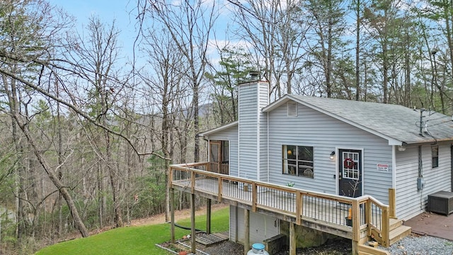 view of side of home with a yard, a chimney, a wooden deck, and roof with shingles