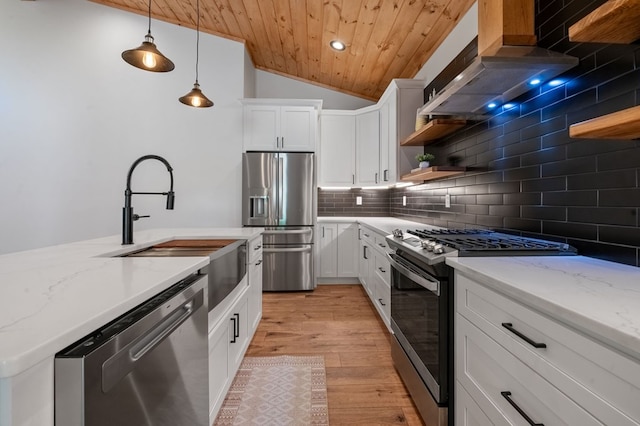 kitchen featuring lofted ceiling, exhaust hood, hanging light fixtures, appliances with stainless steel finishes, and white cabinetry