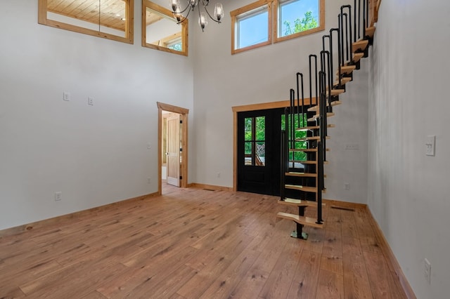 foyer entrance featuring a towering ceiling, wooden ceiling, a notable chandelier, and light wood-type flooring