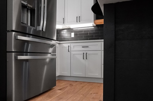 kitchen featuring white cabinets, black refrigerator, decorative backsplash, stainless steel fridge, and light hardwood / wood-style floors