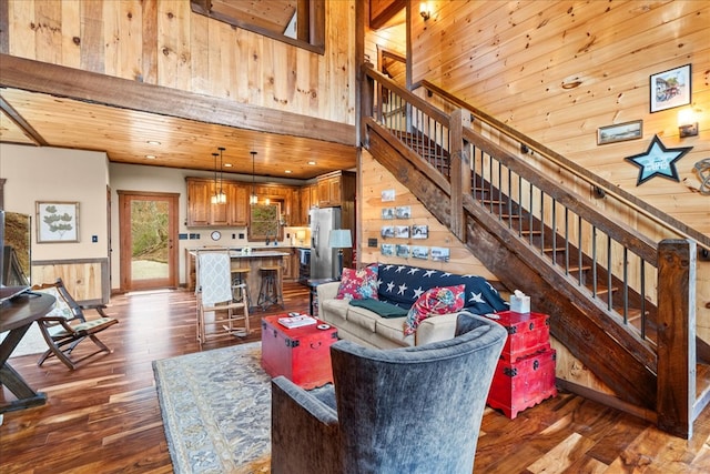 living room featuring wooden walls, dark wood finished floors, wood ceiling, stairs, and a towering ceiling