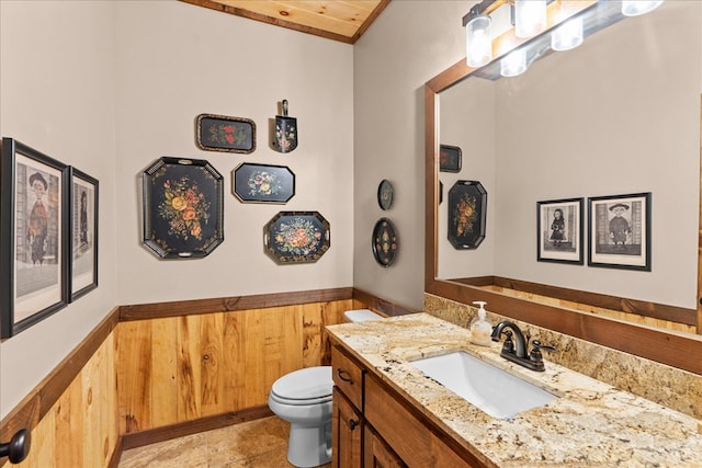 half bath with vanity, toilet, wood walls, and wainscoting