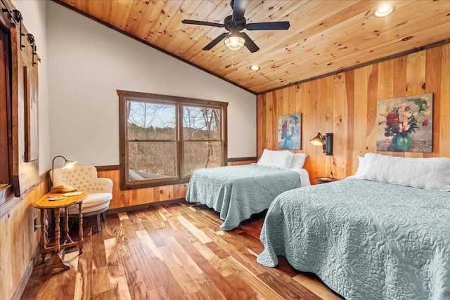 bedroom featuring a wainscoted wall, wood finished floors, a barn door, wooden ceiling, and vaulted ceiling