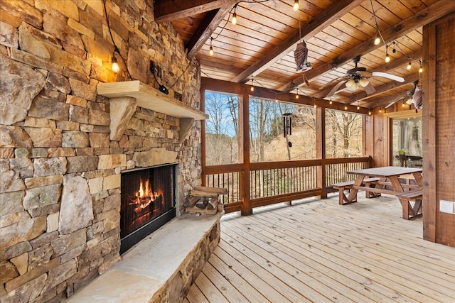 wooden deck with outdoor dining space, an outdoor stone fireplace, and a ceiling fan