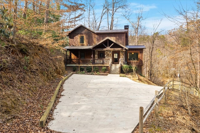 view of front of home featuring covered porch, a chimney, metal roof, stone siding, and a standing seam roof