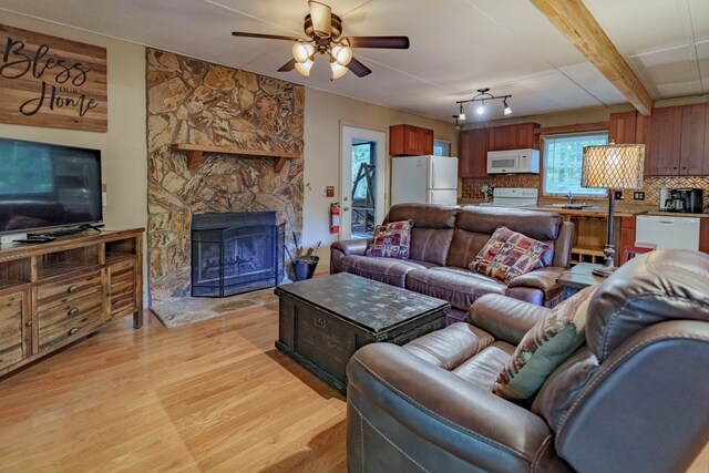 living room featuring a fireplace, beamed ceiling, light hardwood / wood-style flooring, and ceiling fan