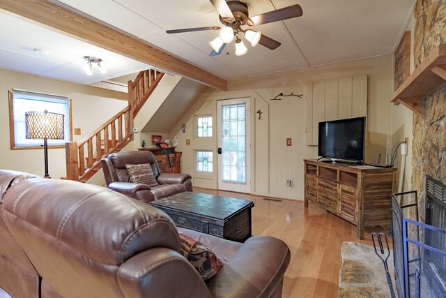 living room with a stone fireplace, ceiling fan, light hardwood / wood-style floors, and beam ceiling