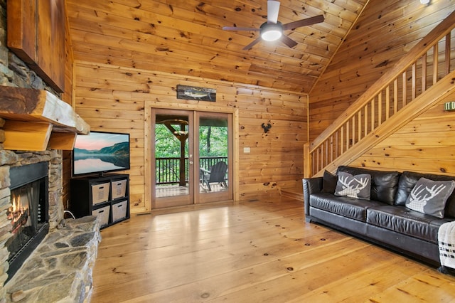 living room featuring wood walls, ceiling fan, a fireplace, and light hardwood / wood-style floors