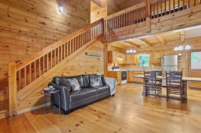 living room featuring a notable chandelier, light hardwood / wood-style flooring, wood walls, wooden ceiling, and beam ceiling