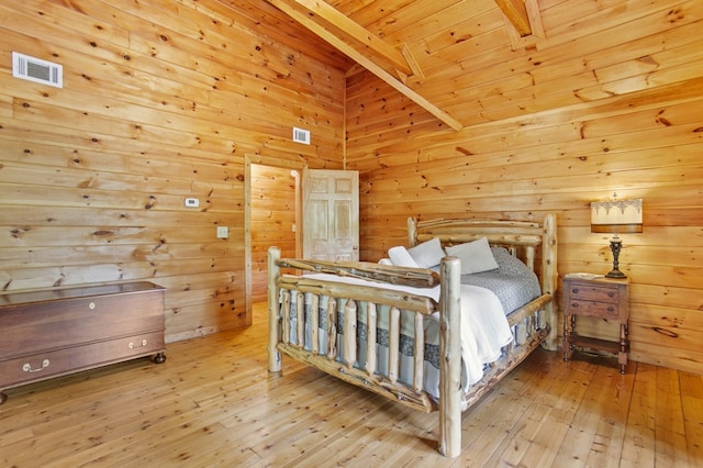 bedroom with light wood-type flooring, wooden walls, and beam ceiling