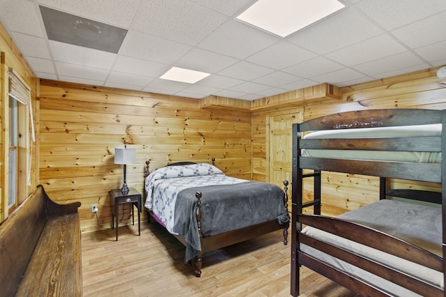 bedroom with light wood-type flooring, wooden walls, and a drop ceiling