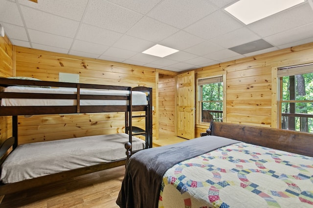 bedroom featuring a paneled ceiling, hardwood / wood-style flooring, and wooden walls