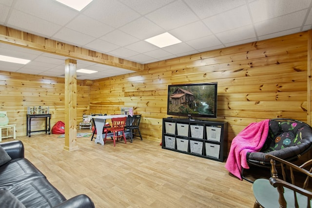 living room featuring wood-type flooring, a paneled ceiling, and wooden walls