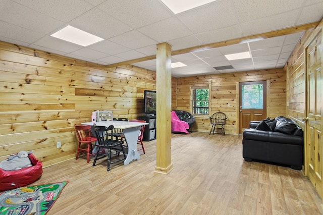 recreation room with a paneled ceiling, wood walls, and light wood-type flooring