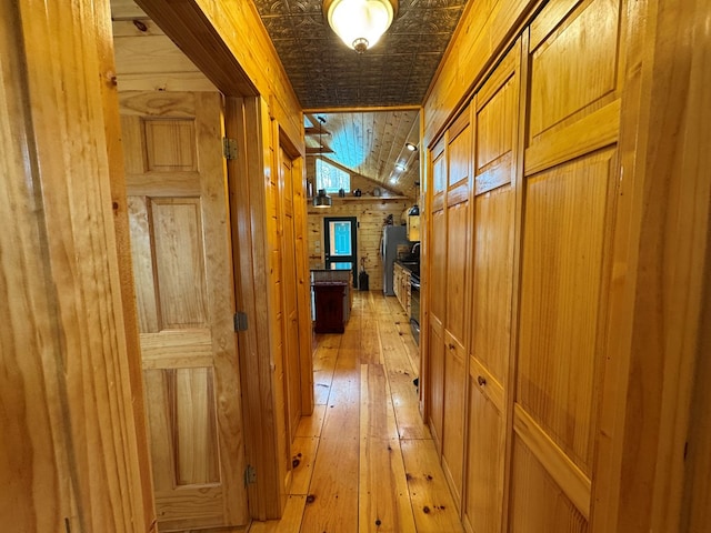 hallway with vaulted ceiling, wooden walls, and light hardwood / wood-style floors