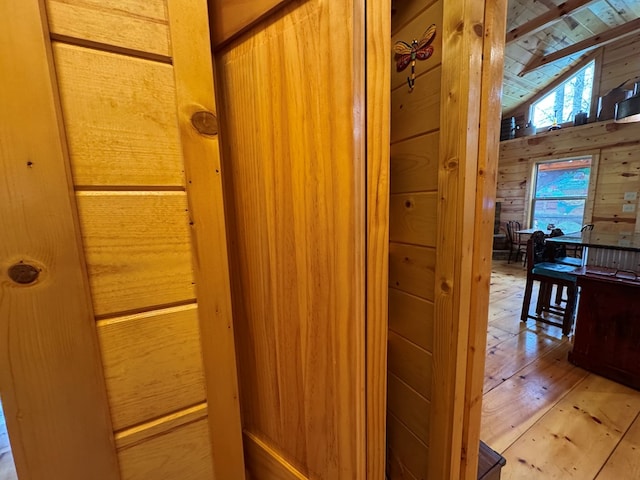 corridor featuring light wood-type flooring, vaulted ceiling, and wood walls