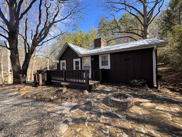 view of front of house featuring a fire pit, a chimney, metal roof, a deck, and board and batten siding