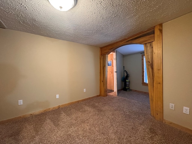 spare room with a textured ceiling, carpet, arched walkways, and baseboards