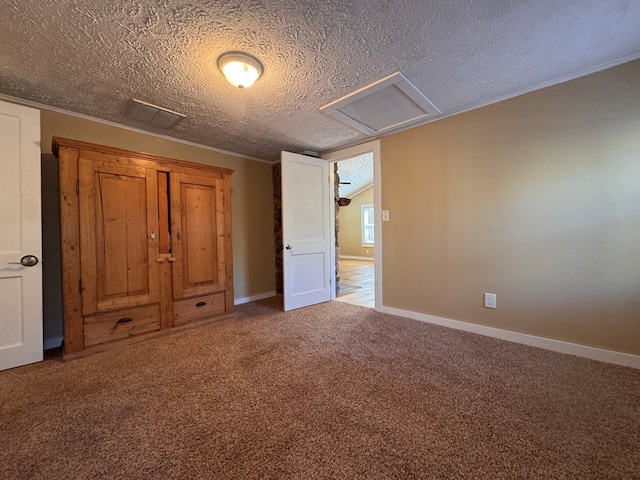 unfurnished bedroom featuring attic access, carpet, a textured ceiling, and baseboards