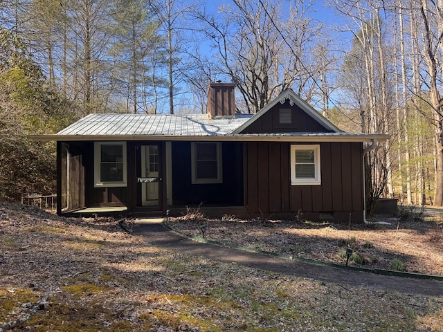 view of front facade featuring board and batten siding, covered porch, metal roof, and a chimney