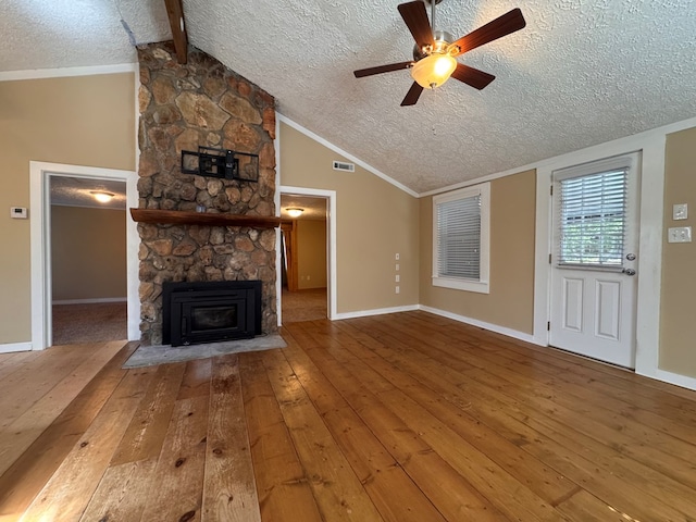 unfurnished living room with lofted ceiling with beams, a stone fireplace, a textured ceiling, and wood-type flooring