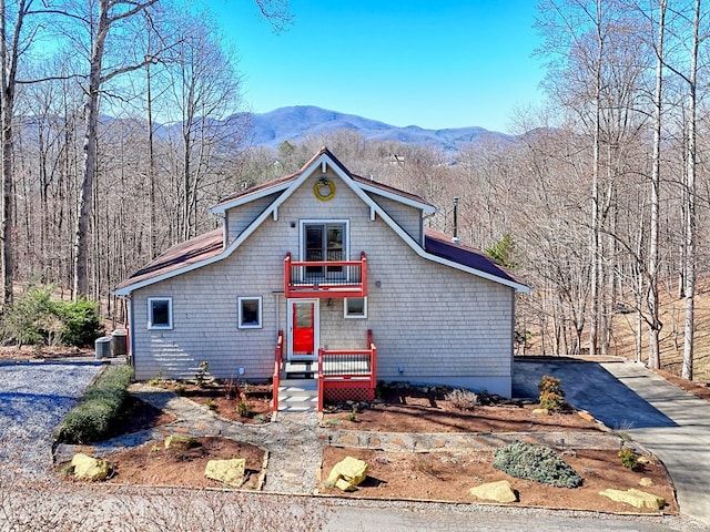 view of front of house with central AC unit, a mountain view, a balcony, driveway, and a forest view