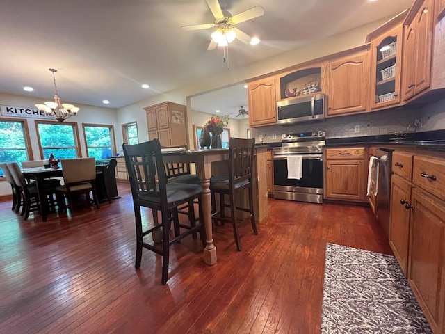 kitchen featuring pendant lighting, backsplash, dark wood-type flooring, ceiling fan with notable chandelier, and stainless steel appliances