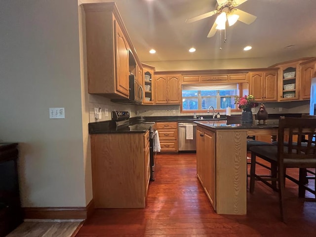 kitchen with a breakfast bar, a center island, ceiling fan, appliances with stainless steel finishes, and dark hardwood / wood-style flooring