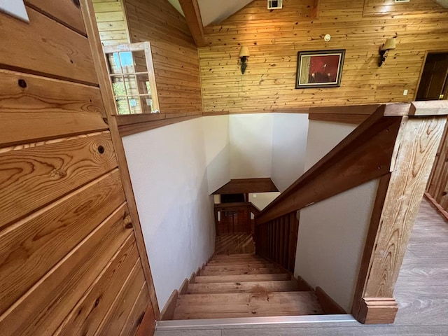 staircase featuring lofted ceiling and wooden walls